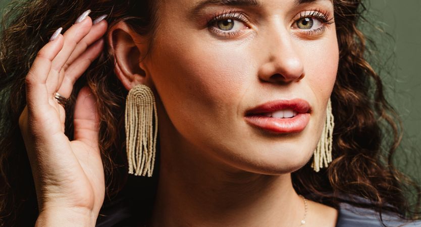 Women wearing tan top with jeans and leather halfmoon bag. she also has two bracelets on - one white and one gold